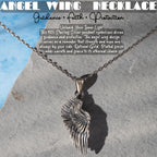 a silver angel wing pendant necklace with a chain, displayed against a gray rock background.
